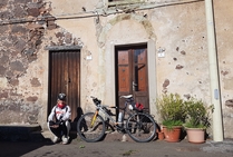 Guest House e bed and break fast in Sardegna, facciata in pietra tipica con ragazza seduta nel gradino della soglia e bicicletta 