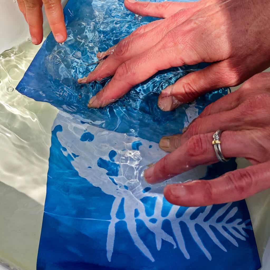 laboratorio di cianotipia mani con foglio stampa sbianca su fondo blufase finale del processo Orablulab