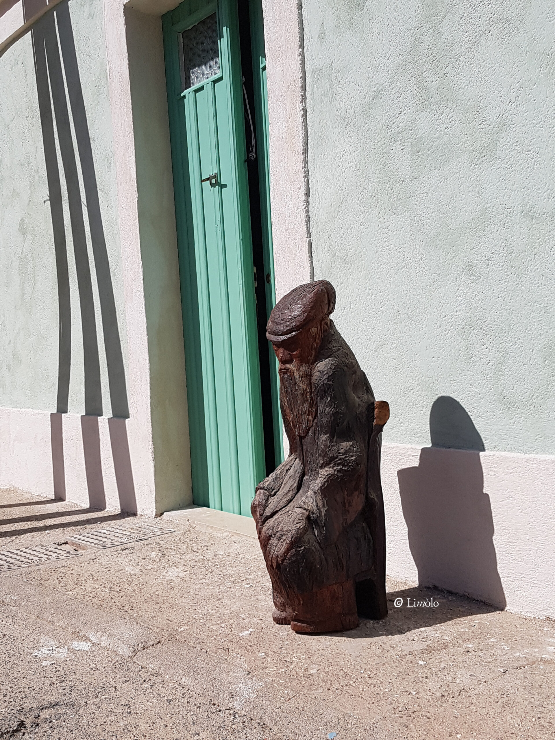 scultura in legno con uomo sardo seduto davanti alla facciata in bioarchitettura di Limolo